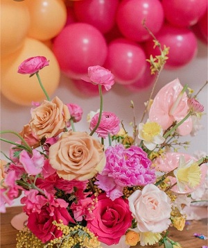 Basket of pink peach white flowers with pink white balloons cluster on top with leaves