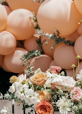 Basket of pink peach white flowers with pink white balloons cluster on top with leaves