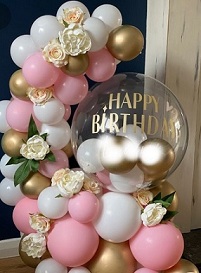 Happy birthday print on the transparent balloon with a garland of 20 small pink white and golden balloons decorated with white flowers at intervals