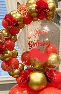 Happy birthday print on the transparent stuffed balloon with small and large red and golden balloons garland decorated with butterflies and red flowers