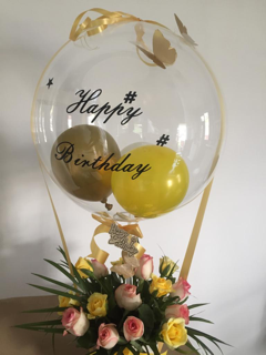 Transparent Balloon with butterflies Printed Happy Birthday stuffed with 2 yellow and gold balloons Tied with ribbons to a basket of 12 yellow and pink roses