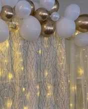 Gold white air blown balloons with string lights and flowers inbetween