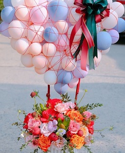 25 Blue Balloons cluster on top held with sticks on a basket of pink blue and yellow roses flowers