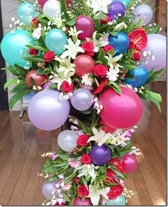 Large Arrangement in 2 tier of Red flowers and white lilies balloons in pink blue with ribbons and roses inserted in between the balloons Approx 3 to 4 feet
