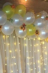 Yellow white air blown balloons with string lights and flowers inbetween