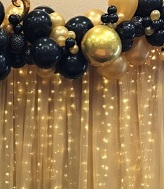 black gold air blown balloons with string lights and flowers inbetween